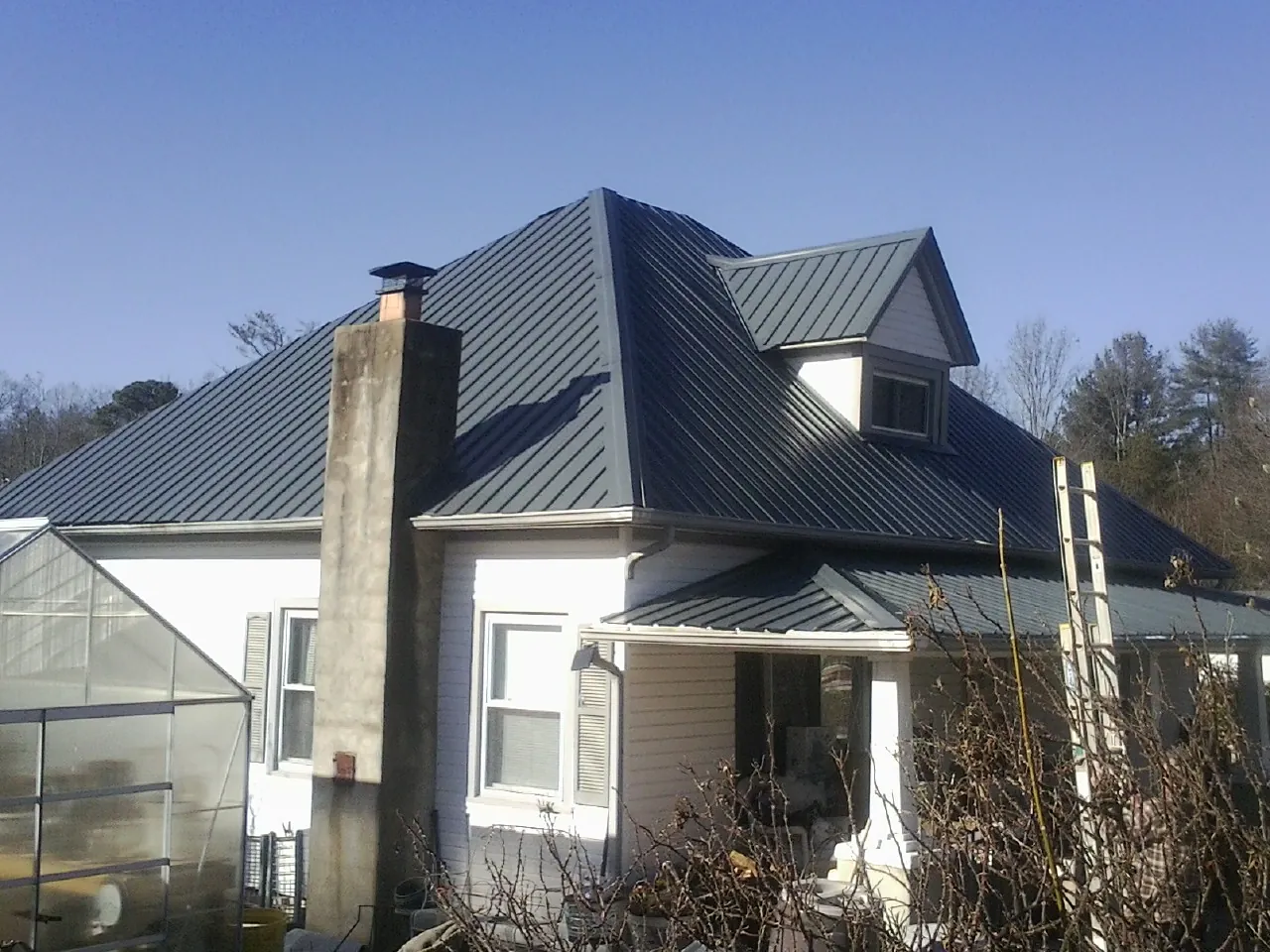 Dark blue standing seam metal roof on a white farmhouse with dormer — Slate & Tile Roof Repair by Roofing Brothers in Stacyville