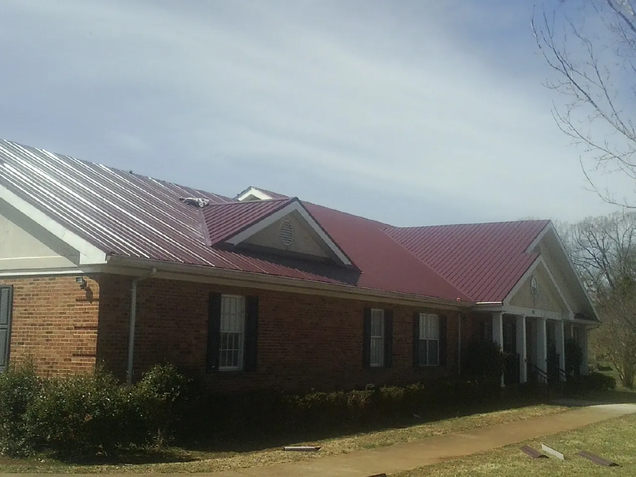 Red metal roof with gabled entries on a long brick building, from a Hail Damage Roof Repair job in Stacyville