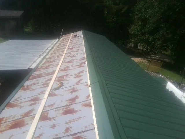 Old rusted panels beside newly installed green metal roofing — Wind Damage Roof Repair by Roofing Brothers in Stacyville