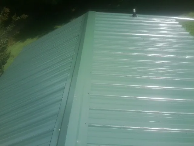 New green metal panels meeting at the ridge of a roof — Flat Roof Repair work by our crew in Stacyville