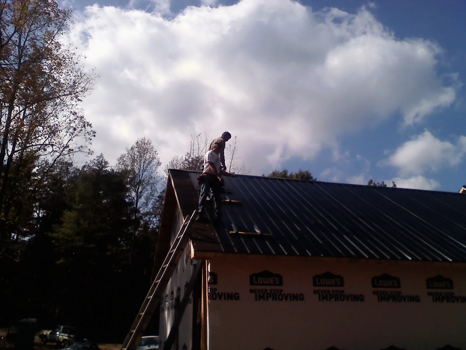 Roofer fastening dark metal panels high against a cloudy sky, from a Roof Inspection job in Stacyville