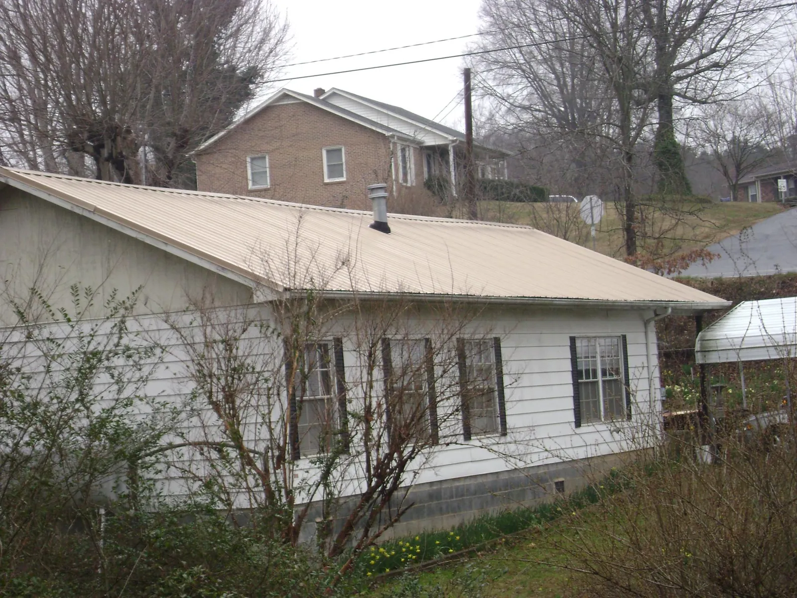 Tan metal roof on a white sided house set into a hillside — Commercial Roofing by Roofing Brothers in Stacyville