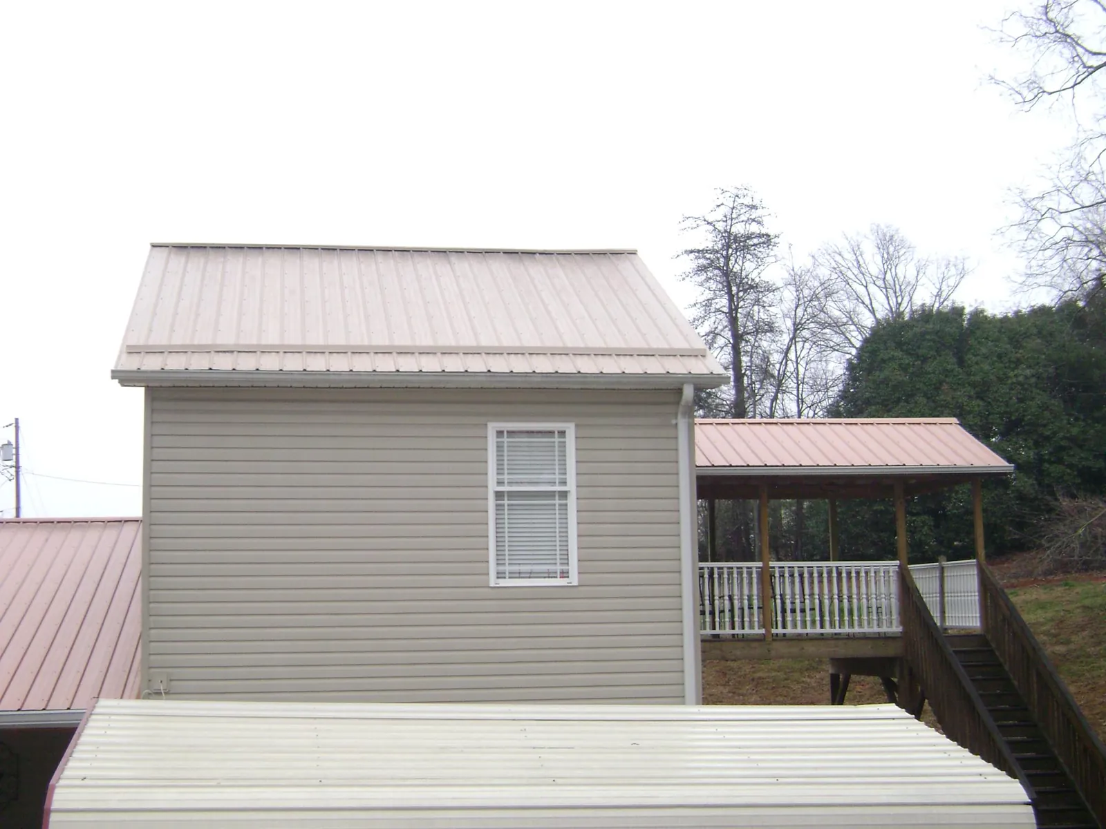 Tan metal roofs on a two story addition and attached porch, from a Roof Replacement job in Stacyville